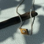 Collier de perles œil-de-grec avec pendentif argenté plaqué or.