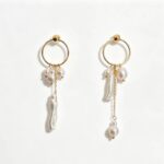 Boucles d'oreilles asymétriques en perles d'eau douce à pompons, mettant en valeur les détails du visage